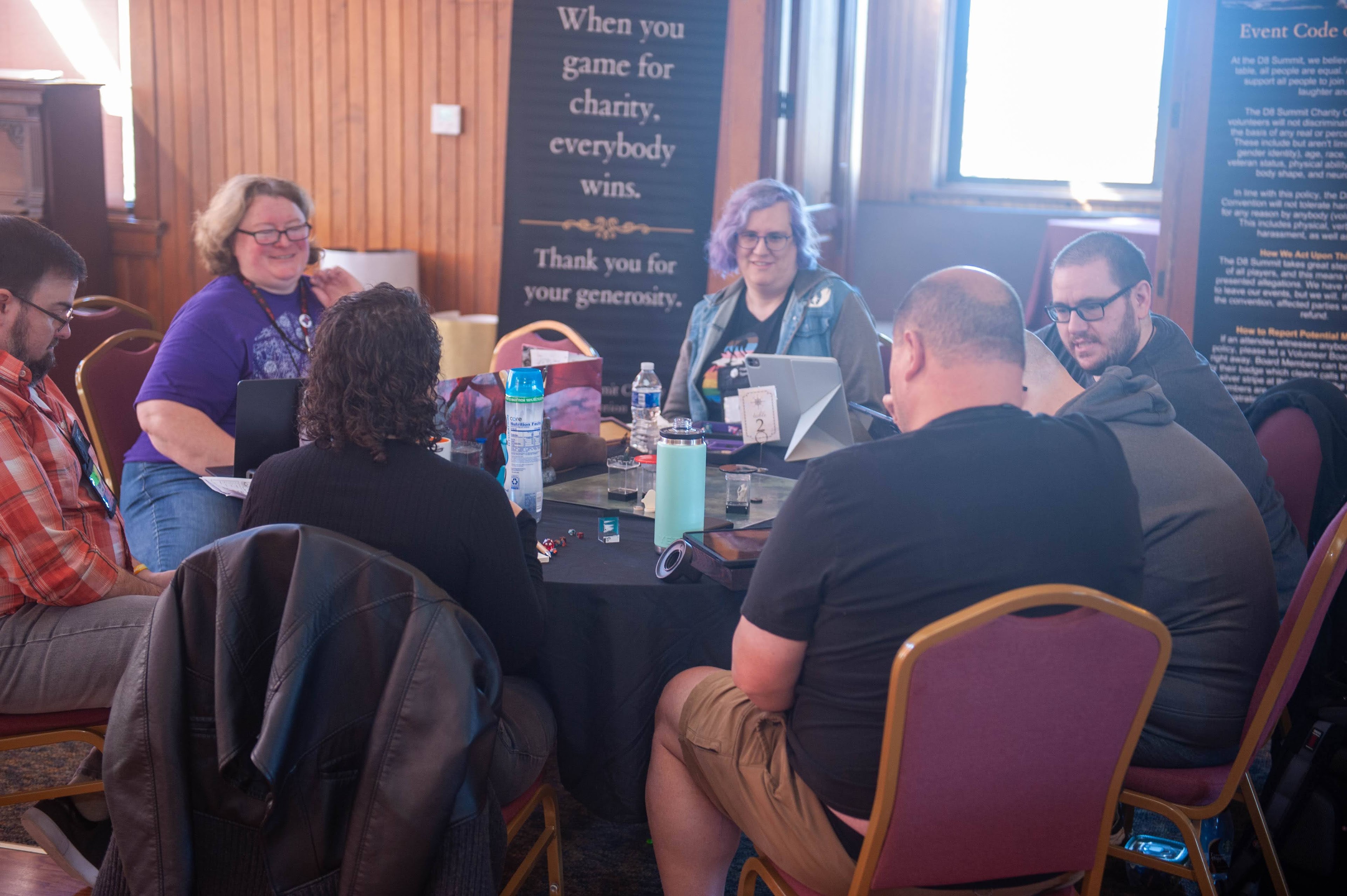 A group of people play D&D around a table at a convention.