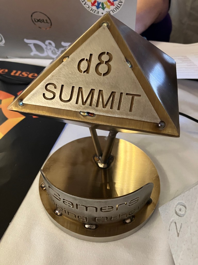 A custom brass desk sculpture featuring the D8 Summit Charities logo